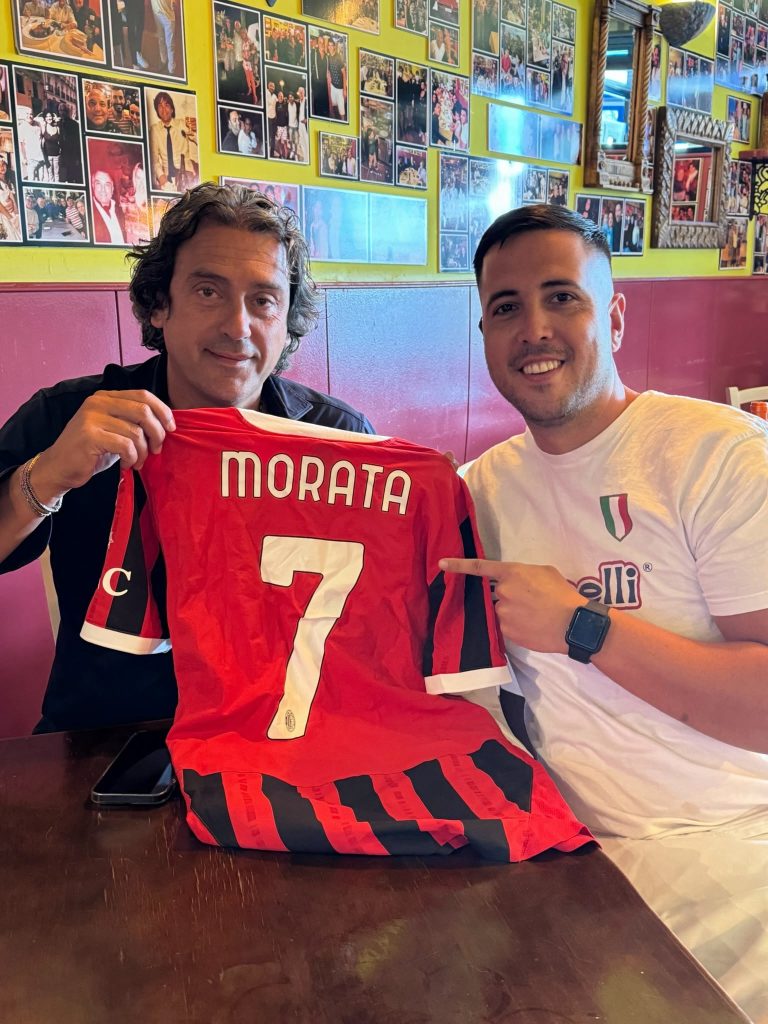 Dos personas sostienen una camiseta de fútbol roja y negra en Bella Napoli