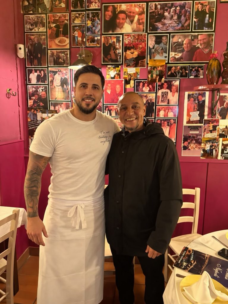 Dos personas posan ante la pared de recuerdos de Bella Napoli